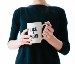 Woman in black shirt holding white mug that says "Like a boss"
